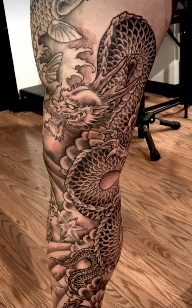 Black and grey Japanese dragon with waves and maple leaves, tattooed down a leg