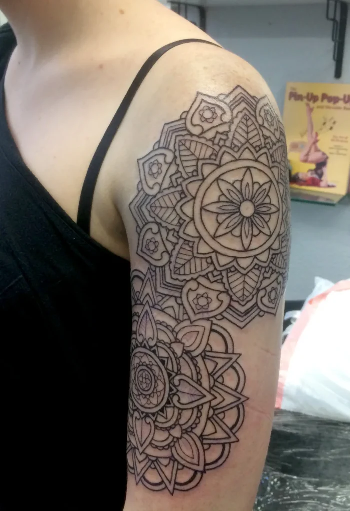 Two mandalas in clean black linework stacked on the shoulder and upper arm